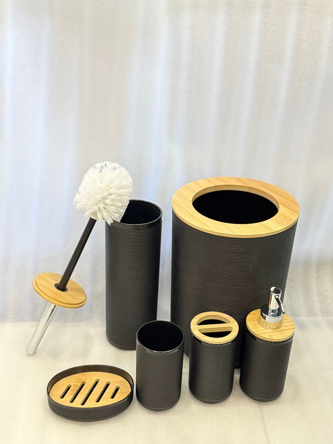 Bathroom accessories set with black and wooden elements on a beige tiled wall background.