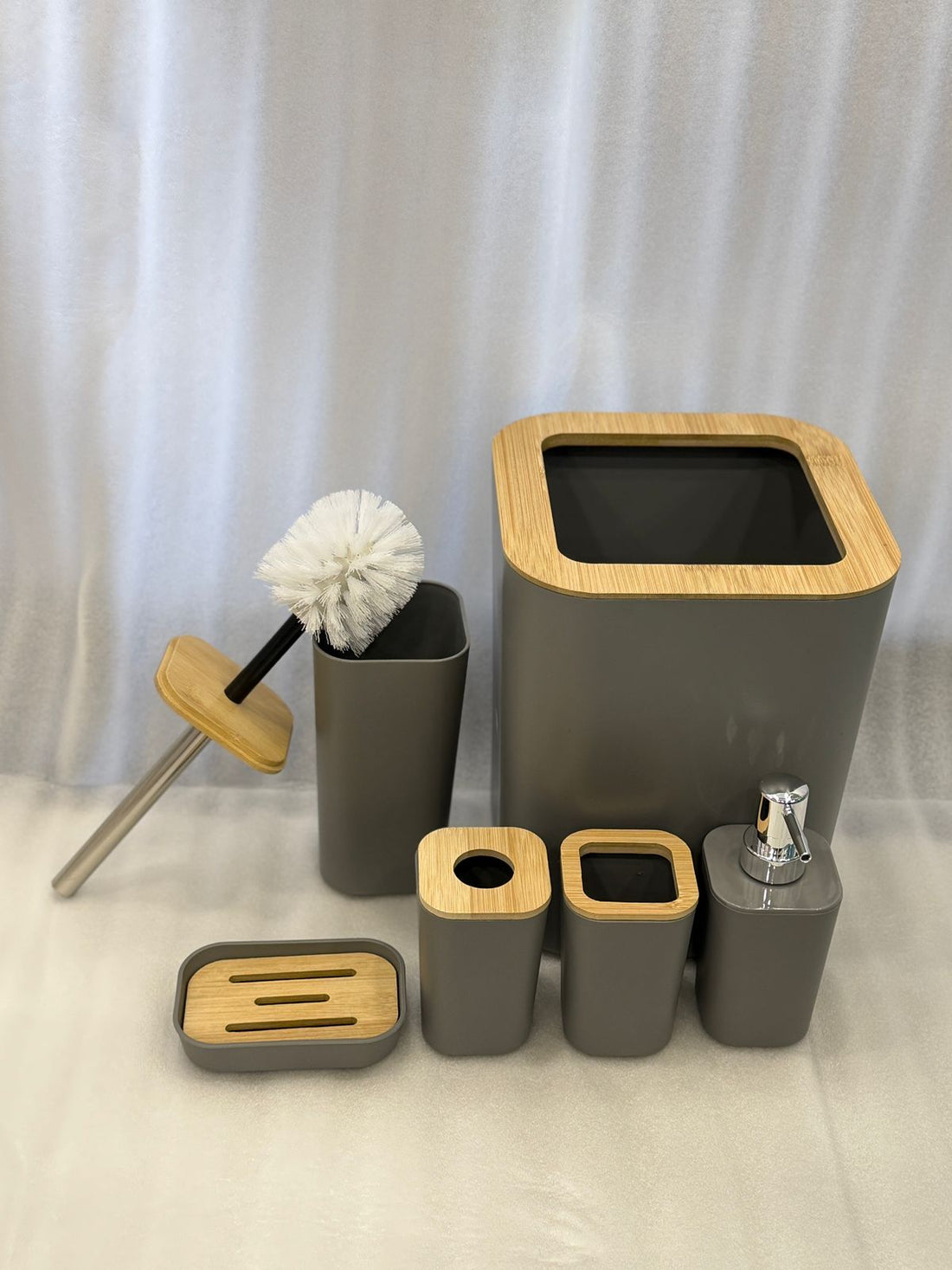 Bathroom accessories set with gray containers and wooden accents on a dark tiled wall.