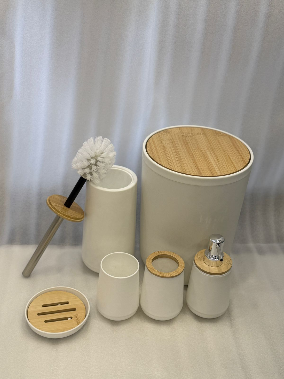 Bathroom accessories set with white containers, wooden lids, and a soap dispenser on a beige tiled wall background.