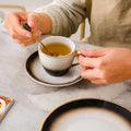 Chai Time in Style – Black & White Tea Cup with Saucer and Spoon, Filled with Tea