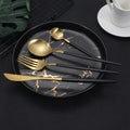 Close-up of the cutlery set arranged on a black and gold plate, emphasizing the premium and stylish finish of the stainless steel pieces.