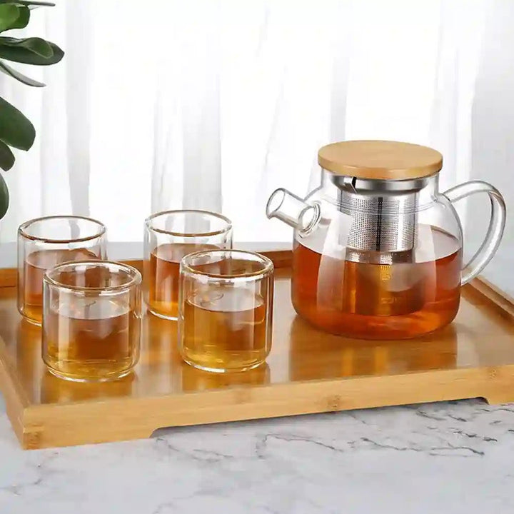 Complete 6-piece glass kettle teapot set displayed on its wooden tray, featuring a half-filled kettle with visible mesh, and 4 glasses filled with tea.