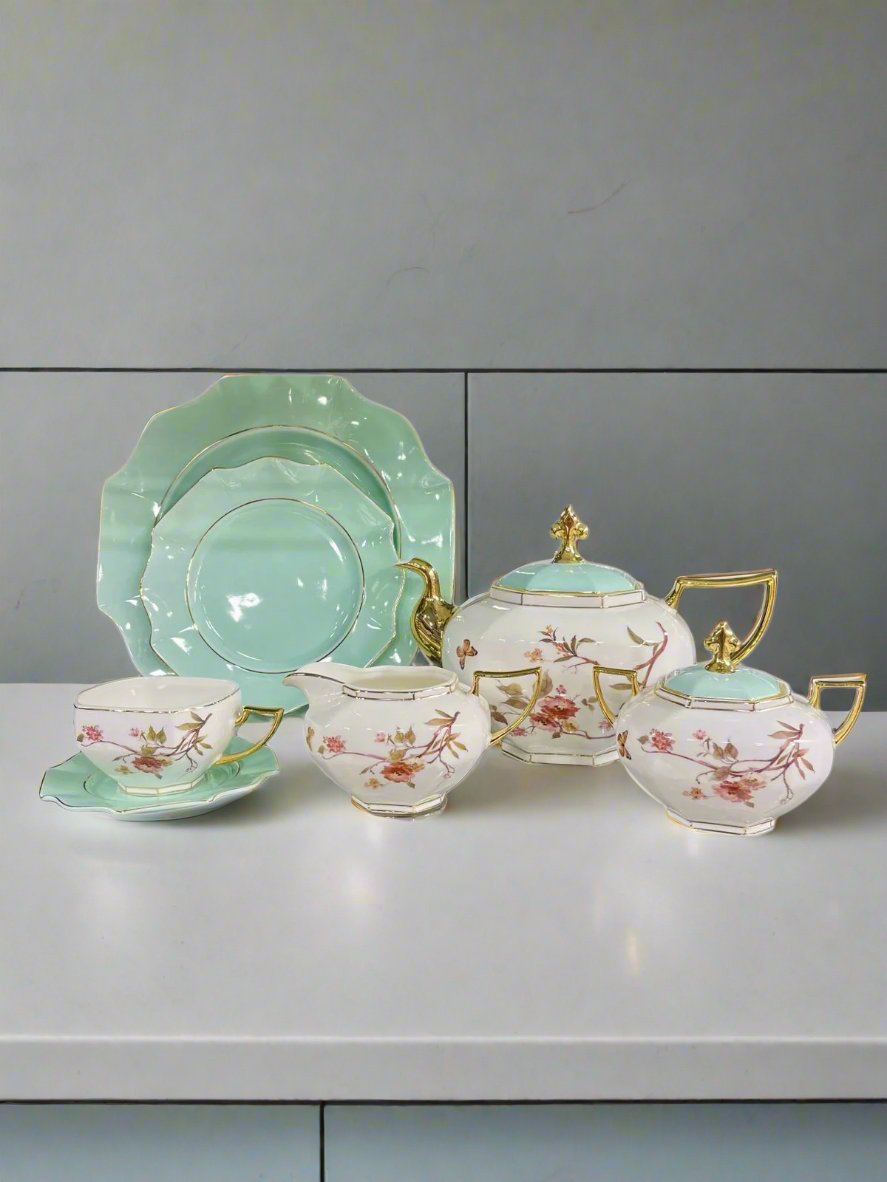 Green ceramic plates with white floral design, accompanied by a white ceramic tea pot, kettle, and sugar pots, all featuring a delicate floral pattern, perfect for an elegant tea set display.