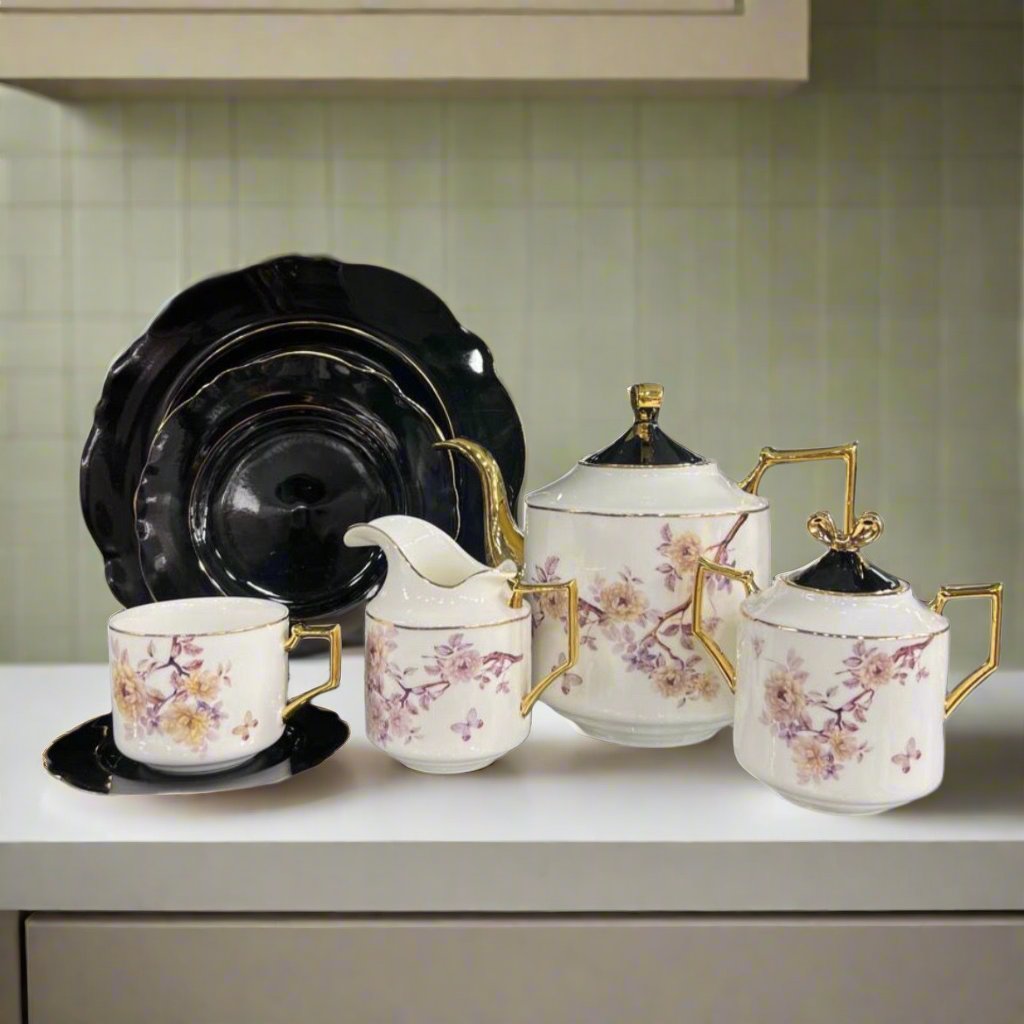 Modern ceramic floral teaset featuring black plates, white teapot, kettle, mugs, and sugar pot with black lids. Elegant floral design perfect for tea settings.