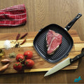 Non-stick aluminium grill pan on a cutting board with raw steak and spices, highlighting its versatility for grilling meat and vegetables.