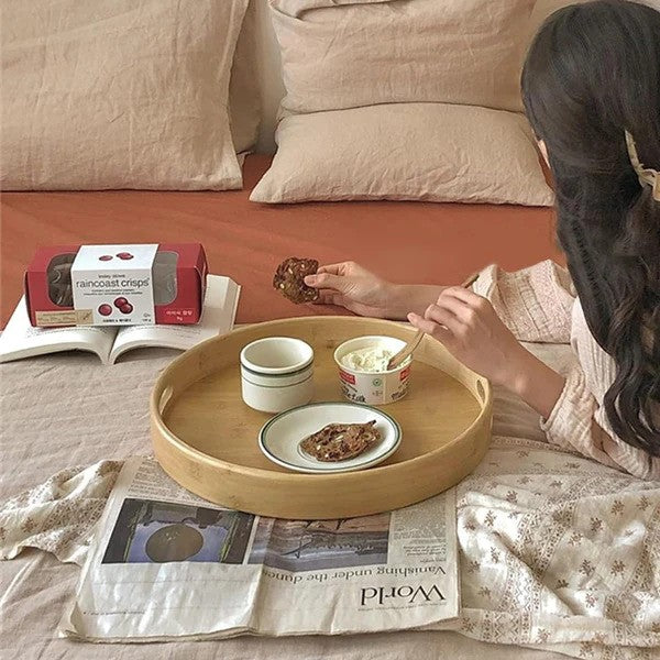 Round bamboo serving tray placed on a bed with ice cream cups arranged on it.