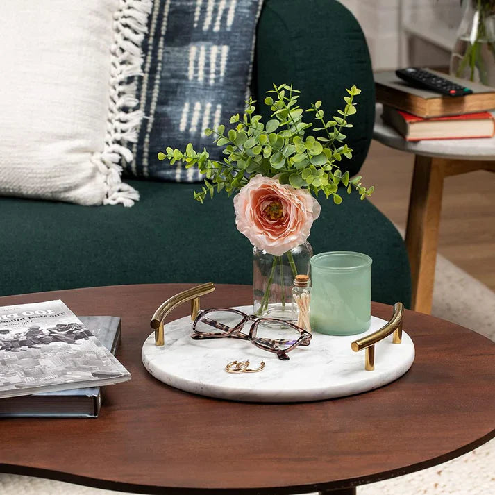 Round marble serving tray from HaulJunction displayed on a living room table with a small flower pot, glasses, toothpick holder, and candle.