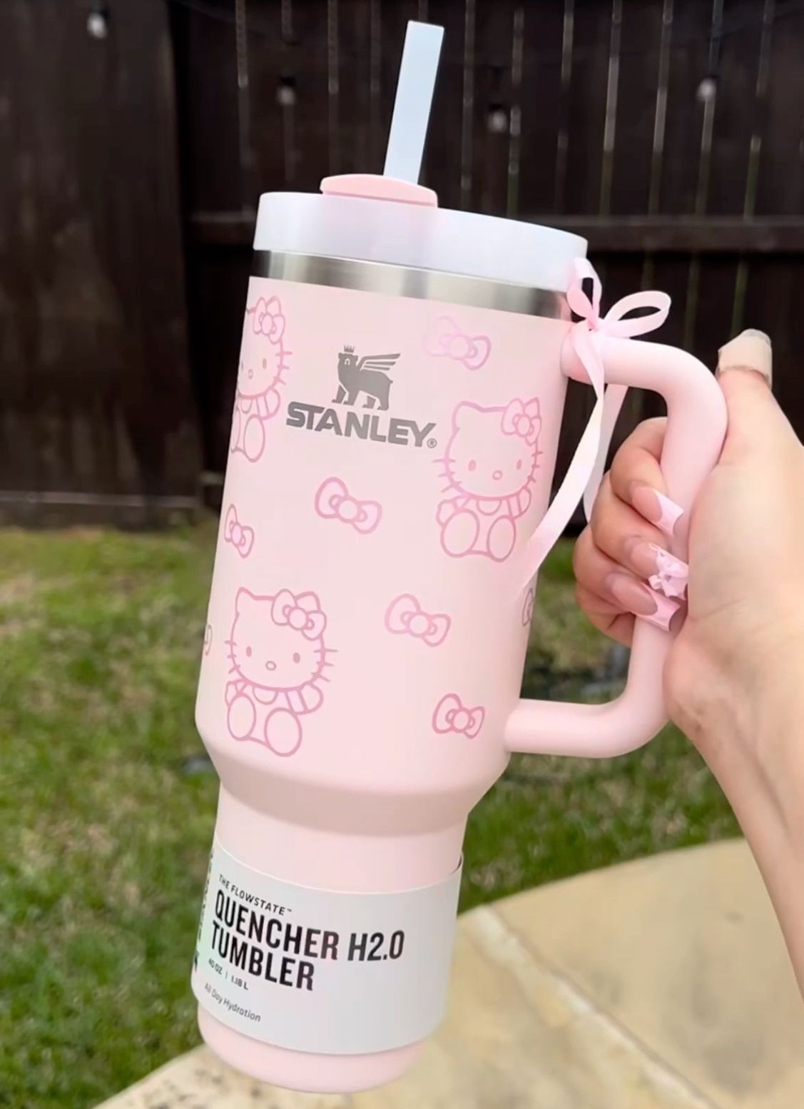A pink Stanley Quencher Tumbler with Hello Kitty design, featuring a straw and a wide handle, being held by a person.
