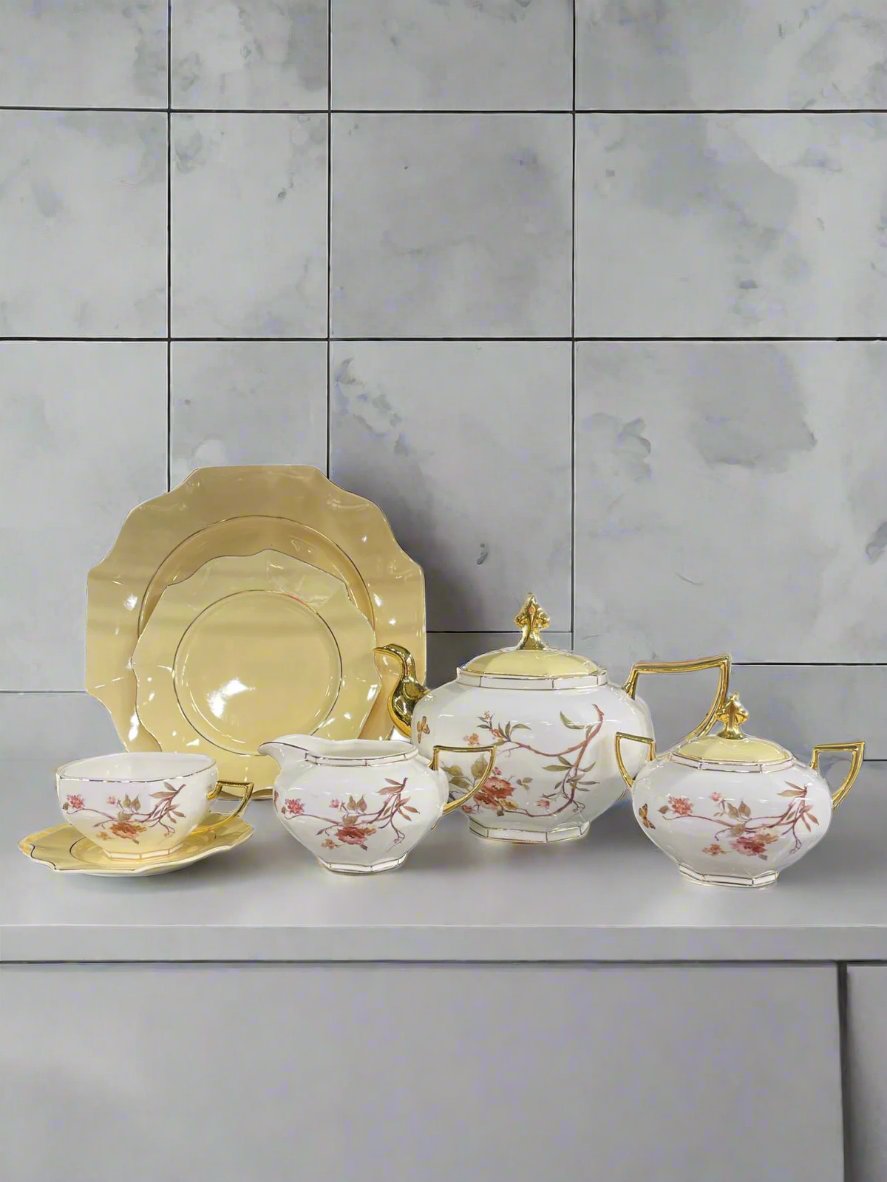 Yellow ceramic plates with white mugs, pot, and kettle, all featuring an elegant floral design, perfect for a cheerful tea set display.