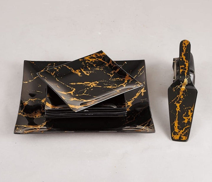 Showcasing a large square cake plate with 6 small square plates placed on top, accompanied by a spatula, all in a black and gold marble design.