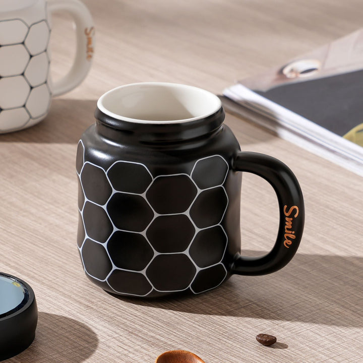 Featuring a black mug with a white honeycomb design on a tabletop, shown with its lid open.