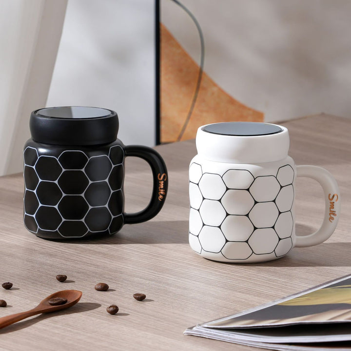 Displaying both black and white smile mugs with honeycomb designs placed side by side on a tabletop.