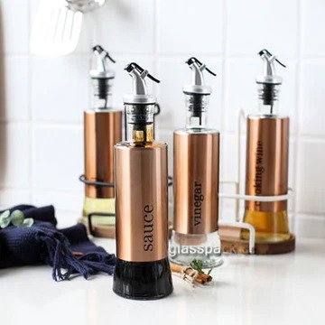  Showcasing 4 gold-finished olive oil bottles with stainless steel covers and glass bottoms on a countertop.