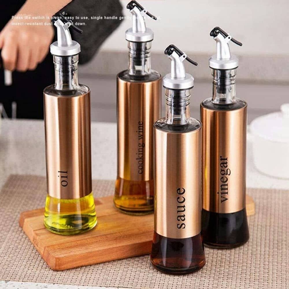 Showcasing 4 gold-finished olive oil bottles with stainless steel covers and glass bottoms on a countertop.