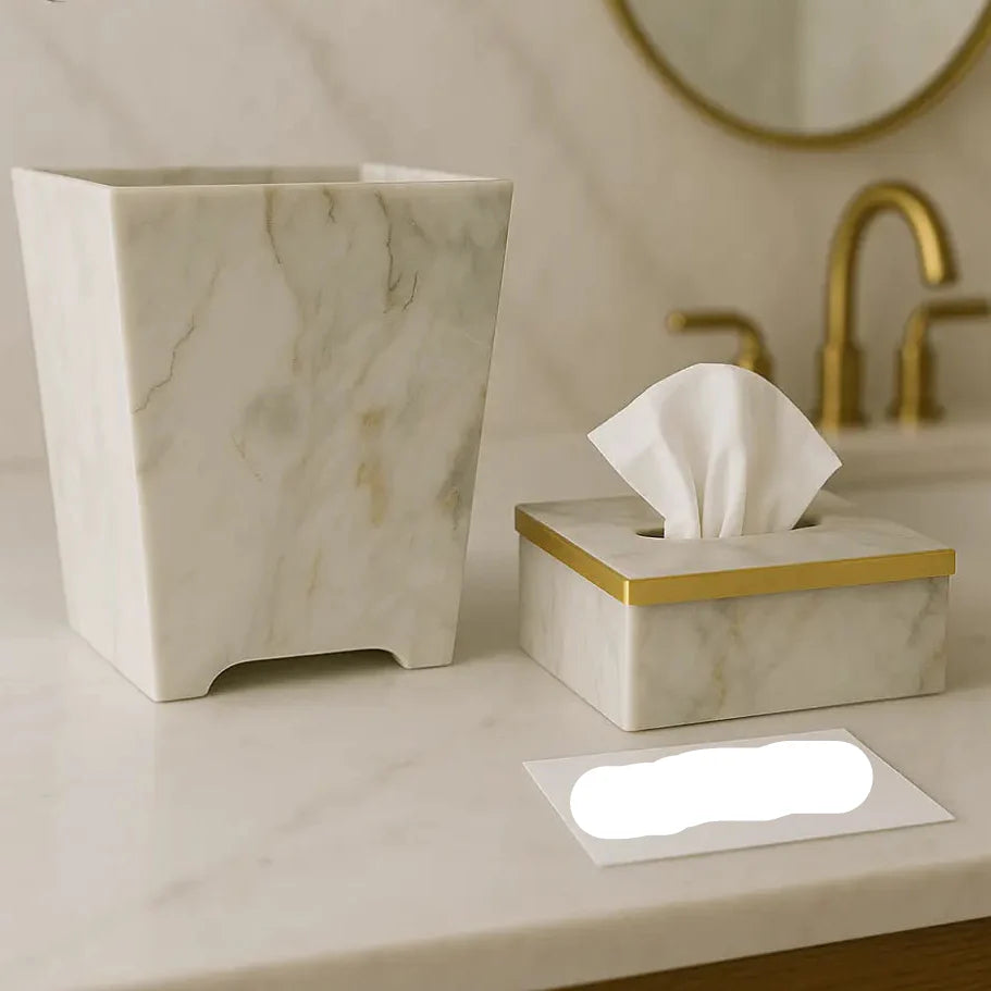 Marble-patterned tissue box and trash can on a bathroom counter with a mirror and faucet in the background.