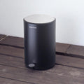 Black trash can with white top on a wooden surface