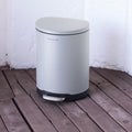 Silver trash can on a wooden floor with a white textured wall background