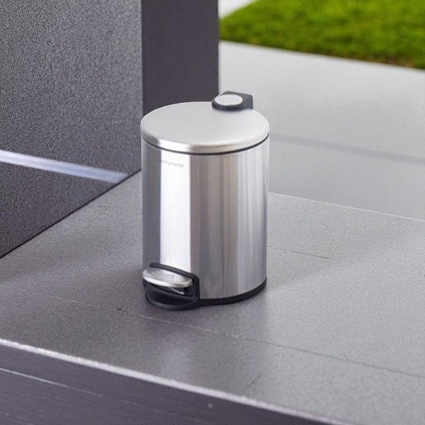 Metallic trash can on a gray surface with a blurred green background