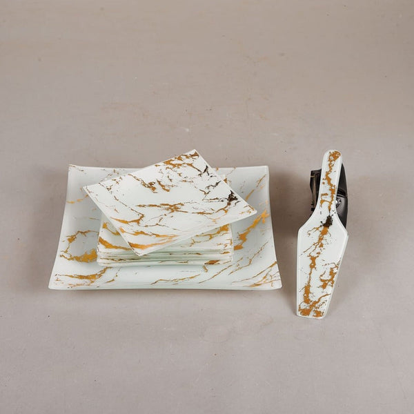 Showcasing a large square cake plate with 6 small square plates placed on top, accompanied by a spatula, all in a white and gold marble design.